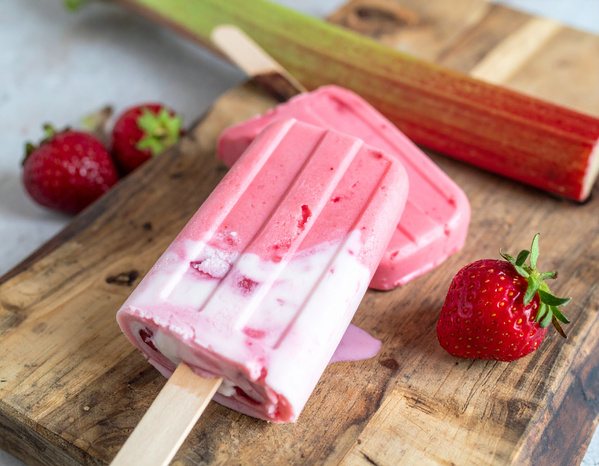KI generiert: Erdbeer-Rhabarber-Eis am Stiel auf Holzbrett mit frischen Erdbeeren.