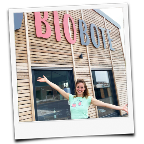 KI generiert: Eine Person posiert fröhlich vor einem Holzgebäude mit dem Schriftzug "BIOBOTE".