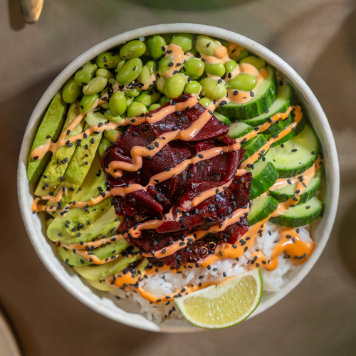 KI generiert: Eine bunte Poké-Bowl mit Toppings wie Avocado, Edamame, Gurke, Roter Bete und Sesam auf Reis.