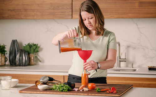 KI generiert: Frau füllt Sauce durch einen Trichter in eine Flasche in moderner Küche.