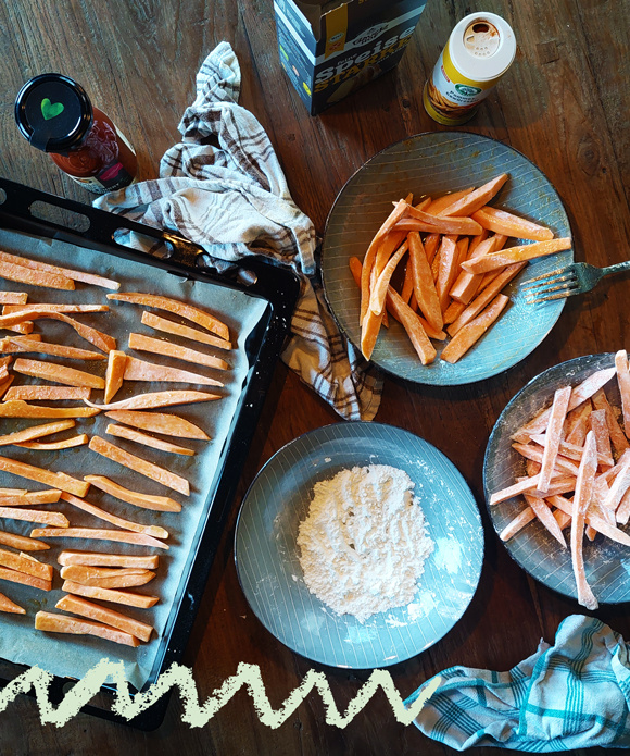 KI generiert: Süßkartoffelsticks werden zubereitet; Zutaten und Backblech sichtbar.