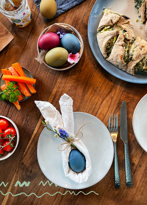 KI generiert: Osterdekoration mit farbigen Eiern, Gemüse und Gebäck auf einem Holztisch.