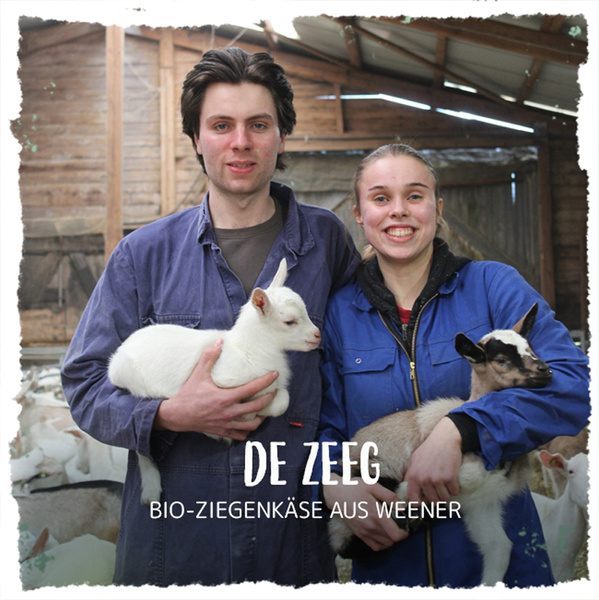 Zwei Personen halten Ziegen in einer Scheune. Text: "DE ZEEG BIO-ZIEGENKÄSE AUS WEENER".