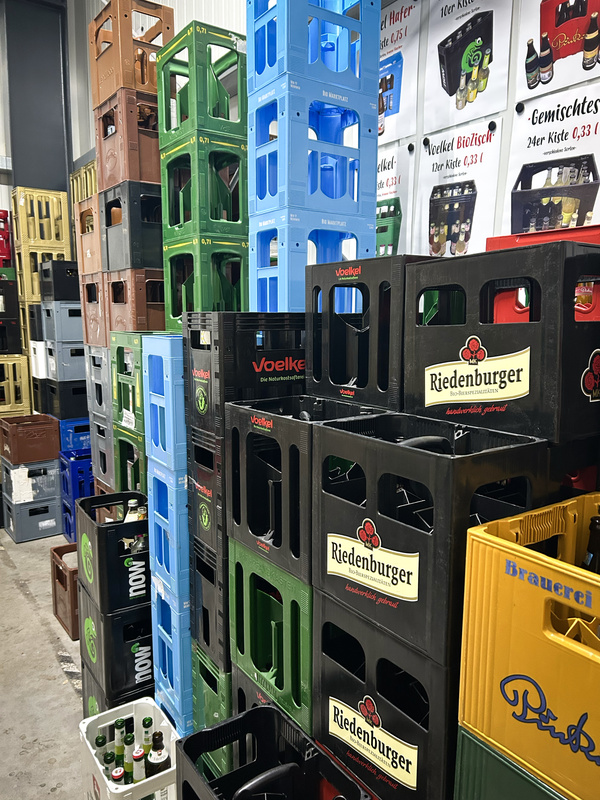 KI generiert: Gestapelte Getränkekisten verschiedener Marken in einer Lagerhalle, mit Postern an der Wand.