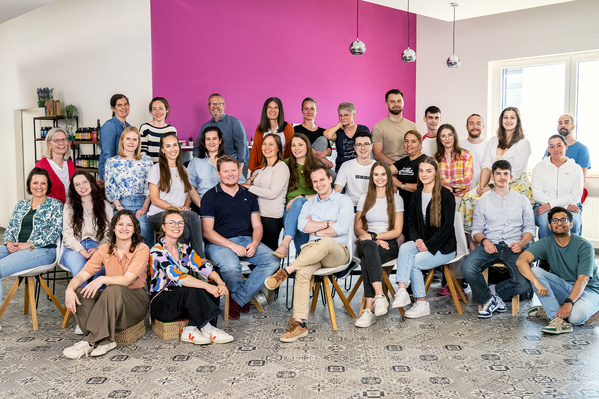 KI generiert: Eine Gruppe von Menschen posiert gemeinsam in einem Raum mit lila Wand.