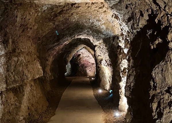 KI generiert: Ein beleuchteter Höhlengang mit unebenen Felswänden und einem schmalen Pfad.