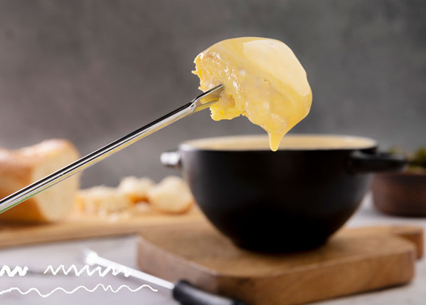 KI generiert: Gabel mit geschmolzenem Käse über einem Fondue-Topf. Im Hintergrund liegt Brot.