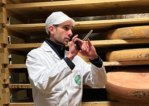 KI generiert: Eine Person im weißen Kittel inspiziert große Käseräder in einem Lagerraum.