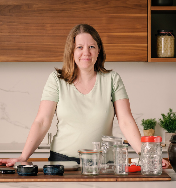 KI generiert: Eine Frau steht in der Küche mit leeren Glasbehältern auf dem Tisch.