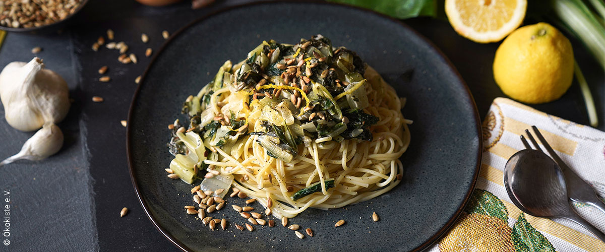KI generiert: Ein Teller Spaghetti mit Gemüse und angerösteten Kernen, dekoriert mit frischen Zitronen und Knoblauch.